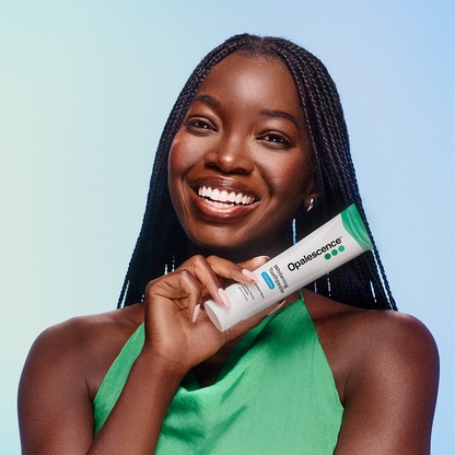 Woman holding a Opalescence teeth whitening product against a light blue background