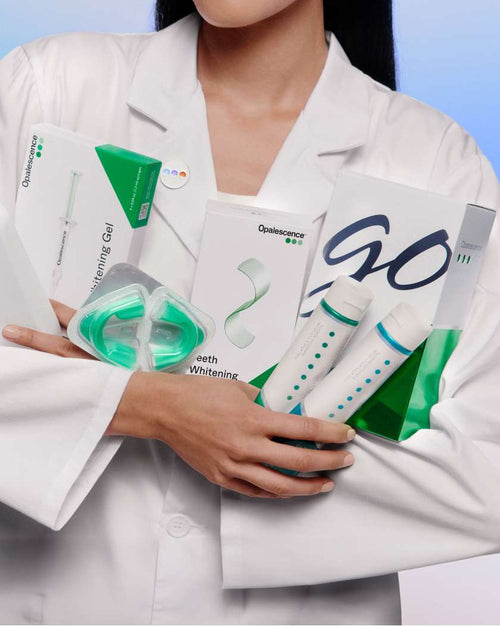 Woman in a white lab coat holding several Opalescence products that come in bundles