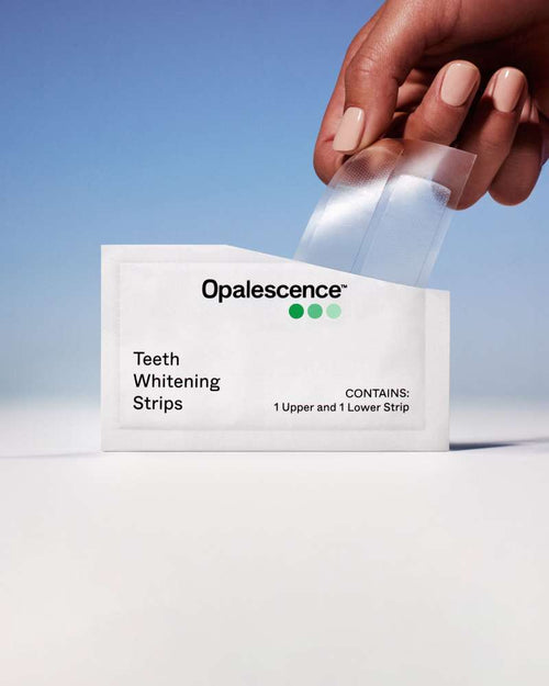 Close up of a hand pulling Opalescence teeth whitening strips from the package