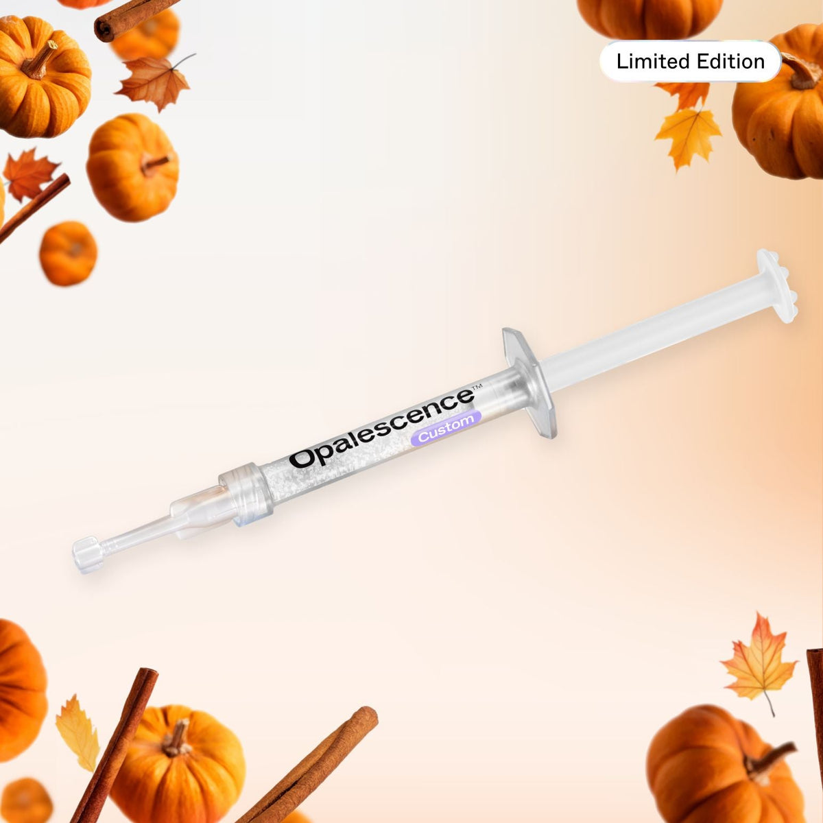 A syringe-style cosmetic applicator labeled Opalescence Custom, shown diagonally on a light peach background with decorative autumn pumpkins, leaves, and cinnamon sticks around the edges. A small 'Limited Edition' badge appears in the top right.