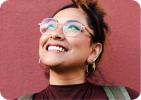 Woman wearing glasses smiling while looking up, standing against a red wall