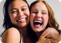 Two women laughing and hugging while looking at the camera