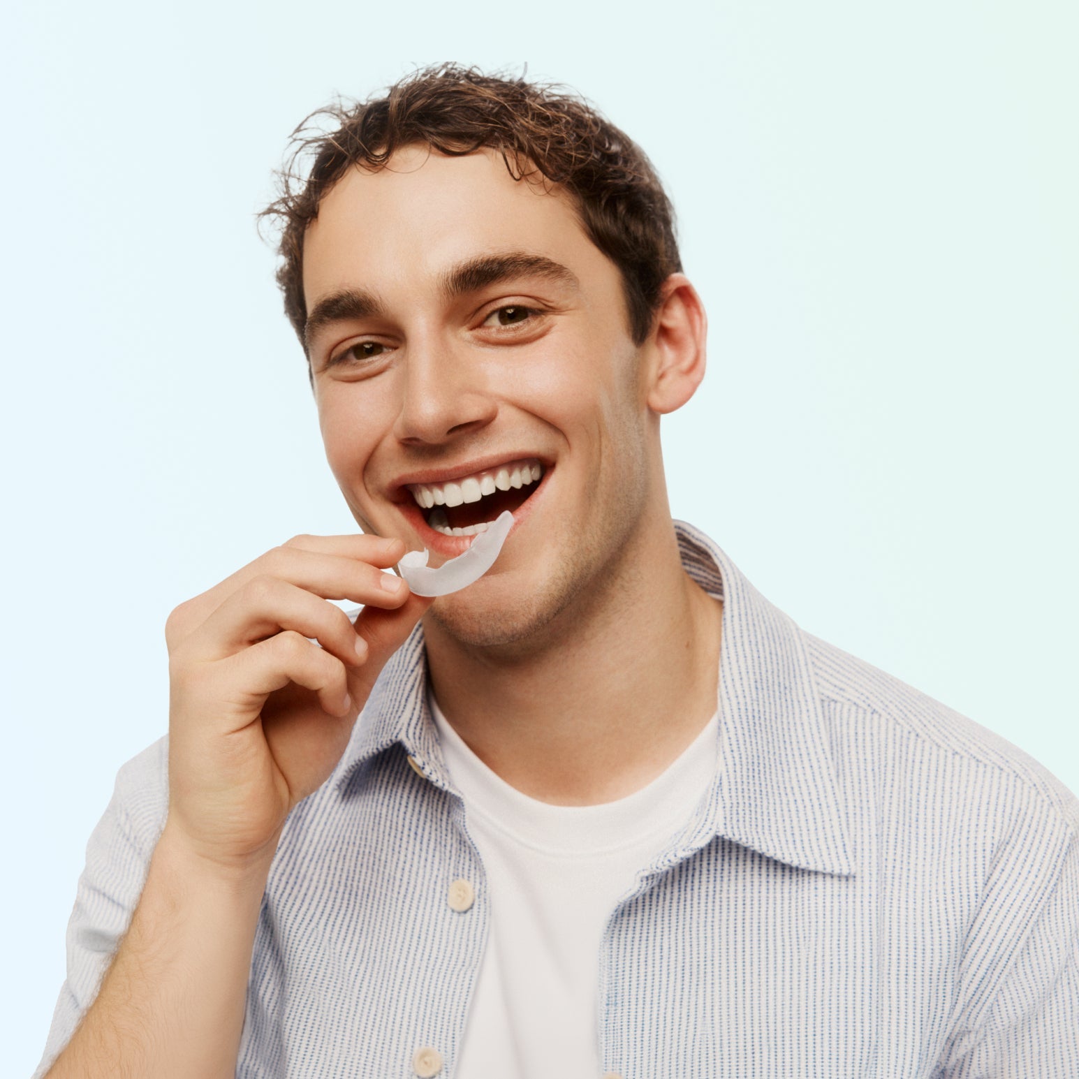 Smiling man holding an Opalescence Go Advanced 15% Prefilled Whitening Tray before placing it on his teeth against a light mint green background.