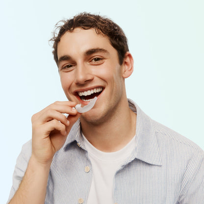 Smiling man holding an Opalescence Go Advanced 15% Prefilled Whitening Tray before placing it on his teeth against a light mint green background.