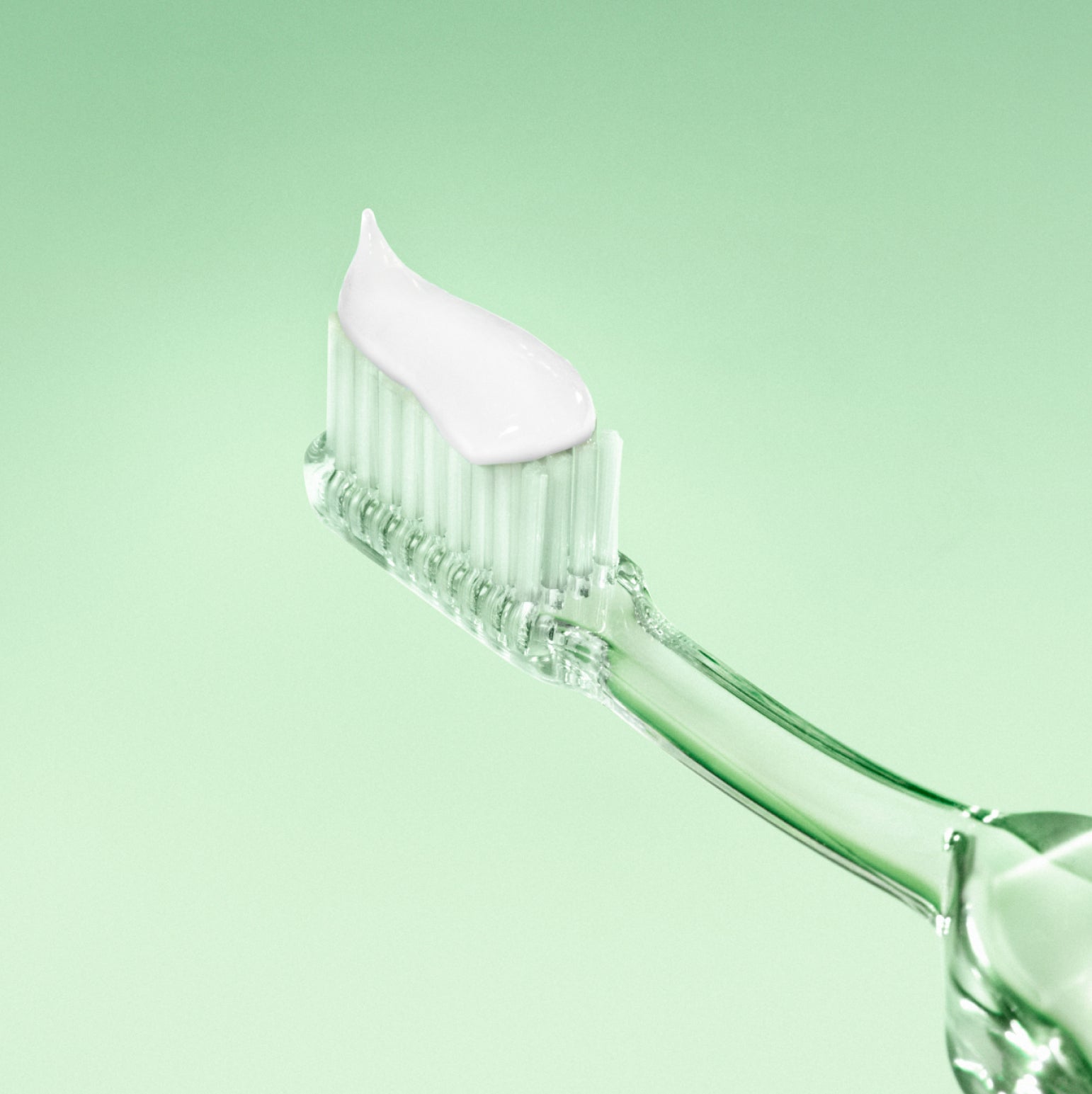 Clear toothbrush with white bristle head on a light green background