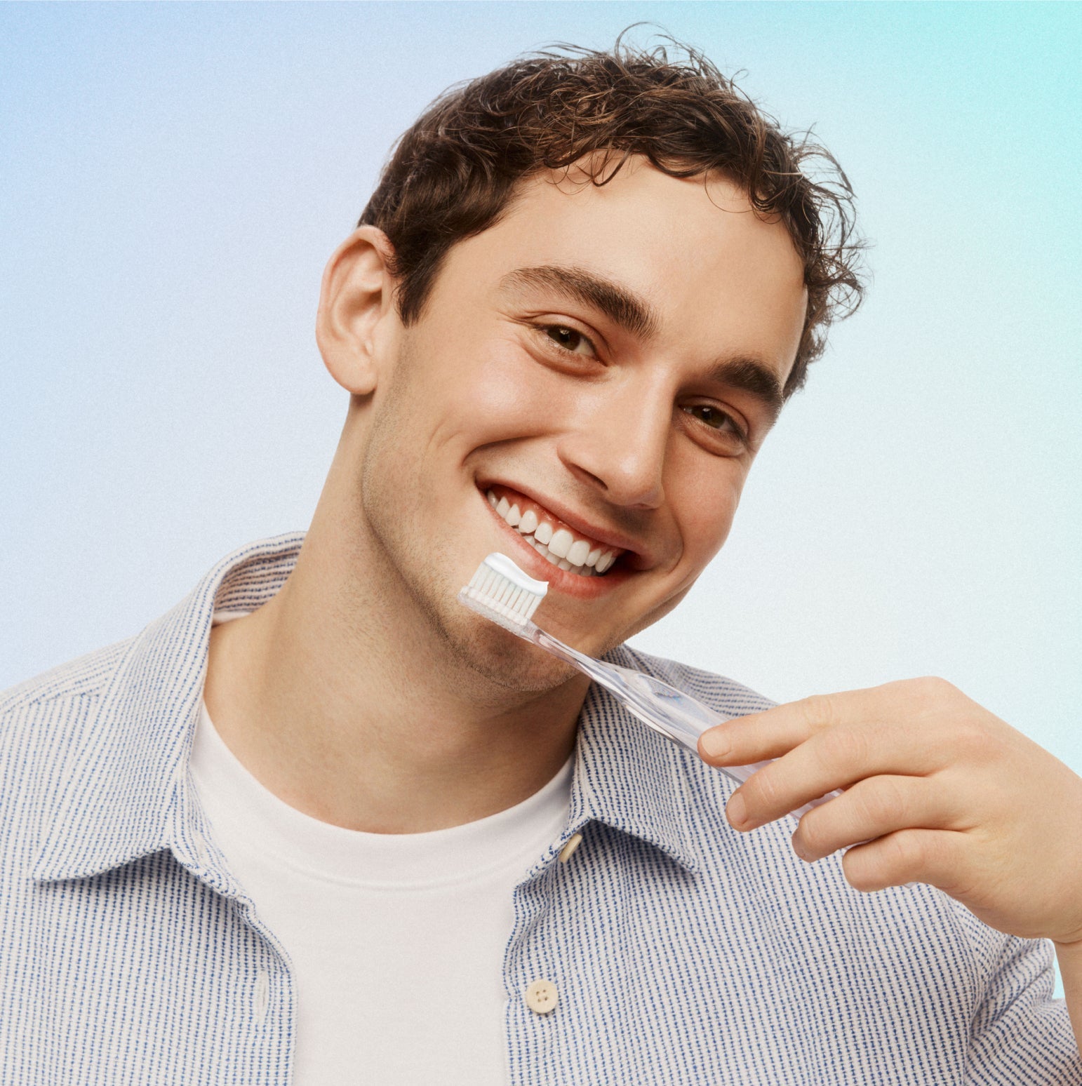 Man brushing his teeth with a clear toothbrush against a light blue background