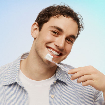 Man brushing his teeth with a clear toothbrush against a light blue background