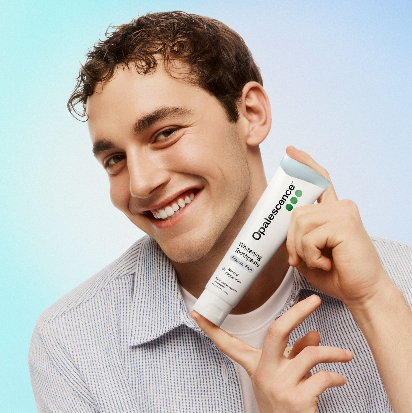 Man holding a tube of Opalescence whitening toothpaste against a light blue background