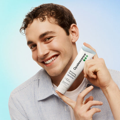 Man holding a tube of Opalescence whitening toothpaste against a light blue background