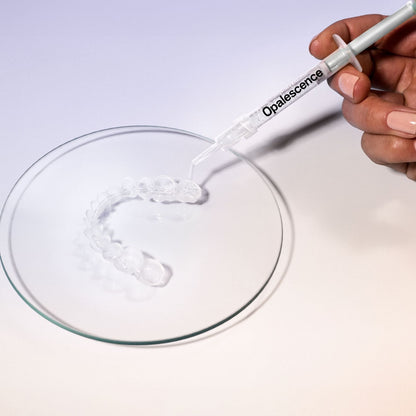 A hand holds a syringe labeled 'Opalescence' over a clear dental tray made of transparent gel, displayed on a clean white background.