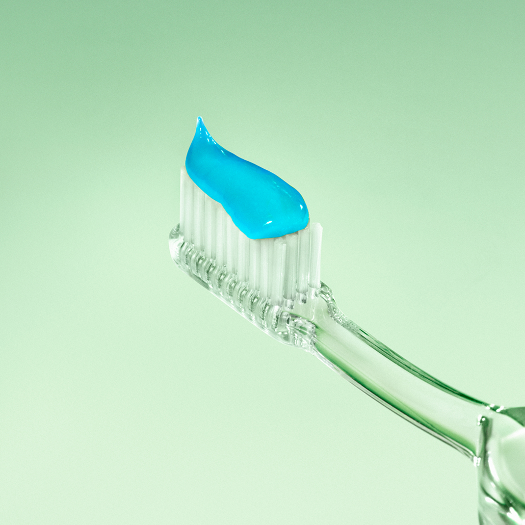 Clear toothbrush with blue toothpaste on a light green background